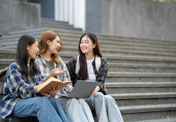 A group of female students with laptops and books while sit on the steps near the campus or university..