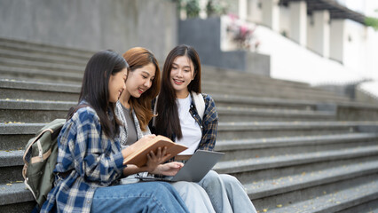 A group of female students with laptops and books while sit on the steps near the campus or university..