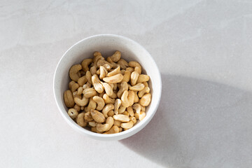 Selective focus flat lay side lit view of cashew nuts in lightly speckled white bowl on ceramic background