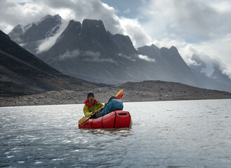A man rowing packraft on Summit Lake, Akshayuk Pass, Baffin Island, Canada - 567766692