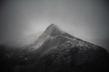 Scienic landscape with rocky mountain top in low clouds in gray cloudy sky. Akshayuk Pass, Baffin Island mountain seen through clouds. mountains background