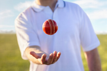 Cricket player bowler throwing up and catching red leather ball ready to bowl - 567768878