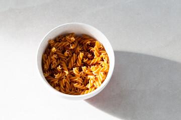 Selective focus flat lay side lit view of uncooked pasta torsades in lightly speckled white bowl on ceramic background