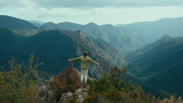 Cinematic woman in traditional sweater hike in mountain. Female hiker reach top of the hill, spread and raise hands in excitement and success. Freedom and joy of travel and outdoor lifestyle.