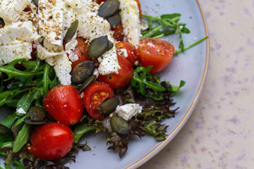 Salad with rucola, feta, cherry tomatoes, pumpkin seeds and sesame on a grey-blue handmade plate