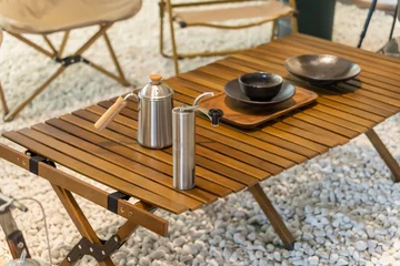  stainless steel kettle, chair,portable gas stove, bowl and vintage lanterns on outdoor wooden table in camping area © xiaoliangge