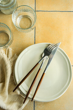 Overhead View Of Plates And Cutlery On A  Tiled Table Next To Glasses, Table Runner And A Jug Of Water