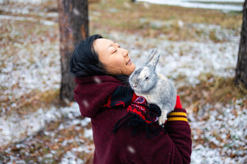 Asian woman standing in the winter magic forest and holding a rabbit in her hands