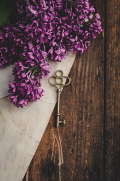 Overhead view of purple lilac flowers, a piece of paper and metal key on a wooden table