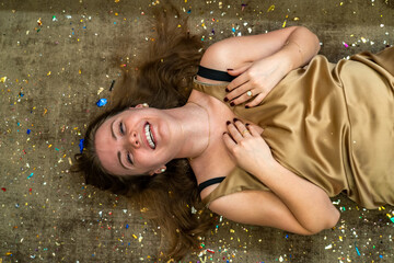 Obraz premium Carefree laughing lady in golden dress lying on floor among confetti