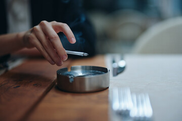 A woman with a cigarette in her hands shakes the ashes into an ashtray, close-up