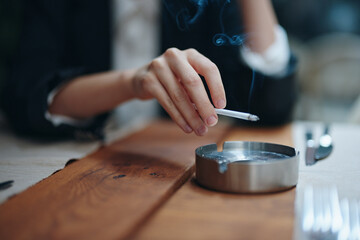 A woman with a cigarette in her hands shakes the ashes into an ashtray, close-up