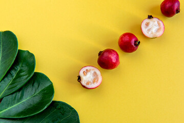 Red cherry guava fruits and leaves on yellow background (Psidium cattleyanum)