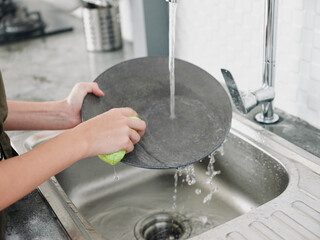 Woman with hands without gloves washes dishes with a dishwashing sponge with bubbles close-up, household chores, no dishwasher, high water consumption. Stylish kitchen design, house cleaning