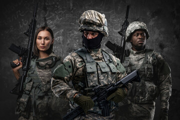 Fototapeta premium Multiethnic military team of three soldiers with rifles against grey background.