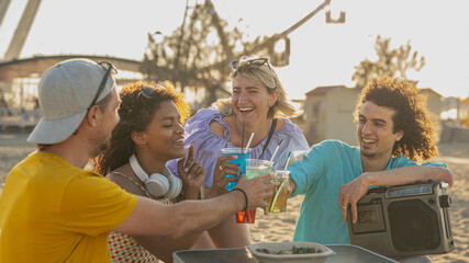Young people toasting with cocktails on a beach party, warm sunset light filter