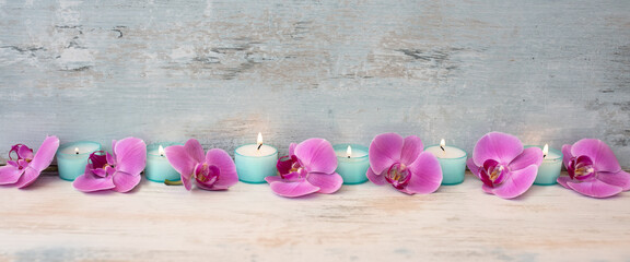 Spa decoration with purple orchids and candle lights in a row on gray vintage wood. Background for wellness and beauty.
