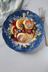 Homemade cottage cheese pancakes with sour cream and blueberries and raspberries and almond leaves in a vintage blue plate