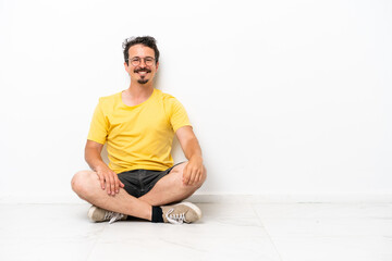 Fototapeta premium Young caucasian man sitting on the floor isolated on white background laughing
