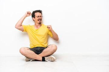 Young caucasian man sitting on the floor isolated on white background celebrating a victory