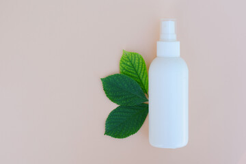 White spray bottle on beige background with leaves and copy space. Organic spa treatment , eco cosmetic products concept.