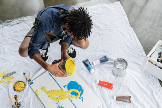 Overhead view of african american artist pouring paint on canvas in studio. - Powered by Adobe