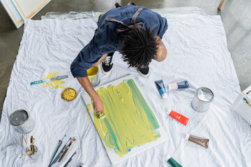 Overhead view of african american artist painting on canvas on floor.