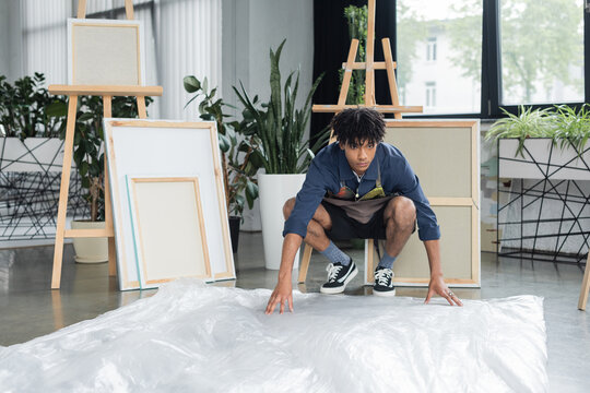 Young african american artist putting cellophane on floor in studio.
