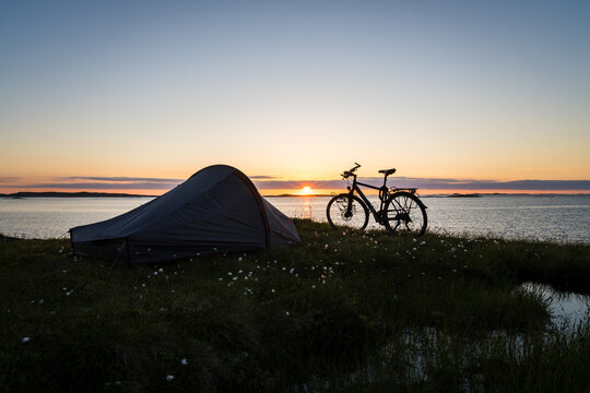 Midnight sun on the island Traena in Norway with bike and tent in the foreground