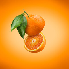 Sliced floating orange fruit with leaves on colorful background.