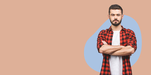 Portrait of happy smiling fashionable handsome man in checkered shirt crossing hands and look at camera isolated over beige background.