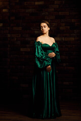 Full-length portraits of a girl in a green dress against a brown brick wall