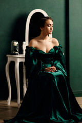 a girl in a green dress sitting against the background of a wall and a mirror