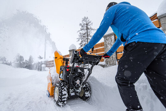 A man with a yellow snow-covered snowblower clears the area from snow. Clearing the access road to the house from snowfall.
