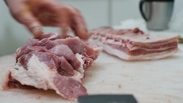 Close-up of a butcher's hands carving a piece of raw meat using a sharp knife and an axe. The worker cuts the meat with a knife and cuts the bone with an axe. meat retail butcher shop