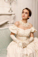 a girl in a vintage beige dress with a necklace on a light wall background