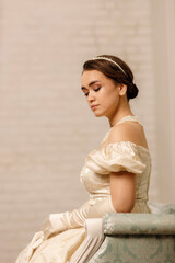 a girl in a vintage beige dress with a necklace on a light wall background