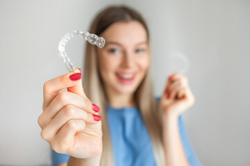 Female hand holding Invisalign, the invisible braces aligner at face woman background. Correction of teeth concept - 567793697