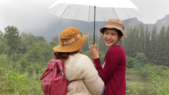 Two Asian women tourists holding umbrellas, smiling, enjoying the beautiful nature. Holiday travel concept. mountain trekking