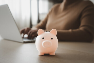 Woman working on laptop beside piggy bank for work and saving concept
