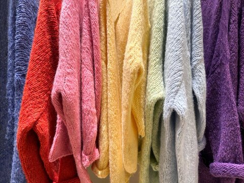 Close-up of assorted multi coloured knitted jumpers hanging in a wardrobe