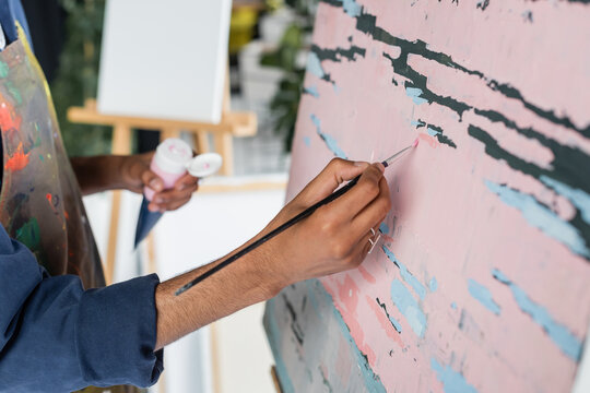 Cropped view of african american artist in apron painting on canvas in studio.