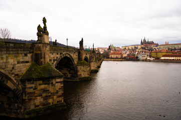 Fototapeta na wymiar A view from the bank of the Vltava to the Charles Bridge, the Old Town Bridge Tower and other monuments of Prague, with swans swimming on the river on a cold winter day