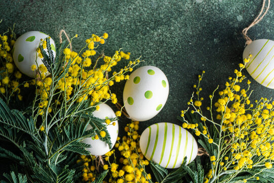 Overhead view of painted Easter eggs with yellow mimosa flowers on a table