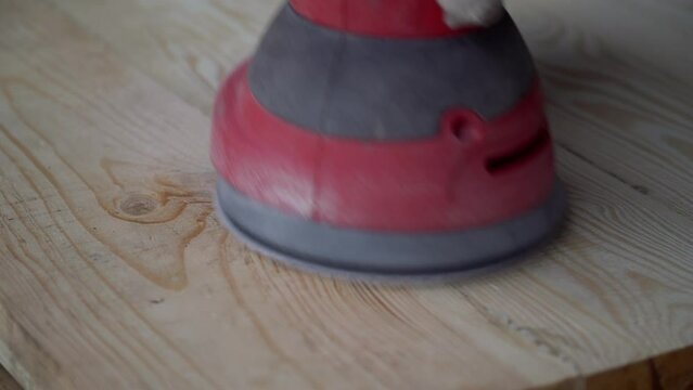 Close up male carpenter grinding wood with orbital sander in workshop. Concept of woodworking with an electric tool