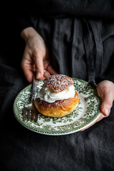 Woman holding vintage plate with homemade semla bun with frangipane and whipped cream.