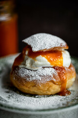 Homemade semla bun with frangipane, apricot jam and whipped cream on vintage plate.