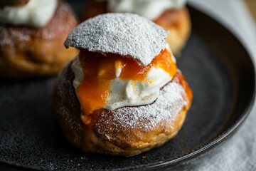 Homemade semla bun with frangipane, apricot jam and whipped cream on vintage plate.