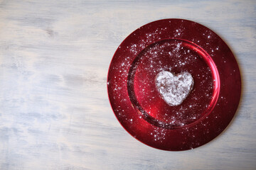Pequeño pastel glaseado en forma de corazón en un plato rojo sobre madera blanca rústica
