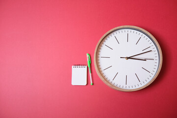 Reloj aislado sobre fondo magenta con libreta y bolígrafo